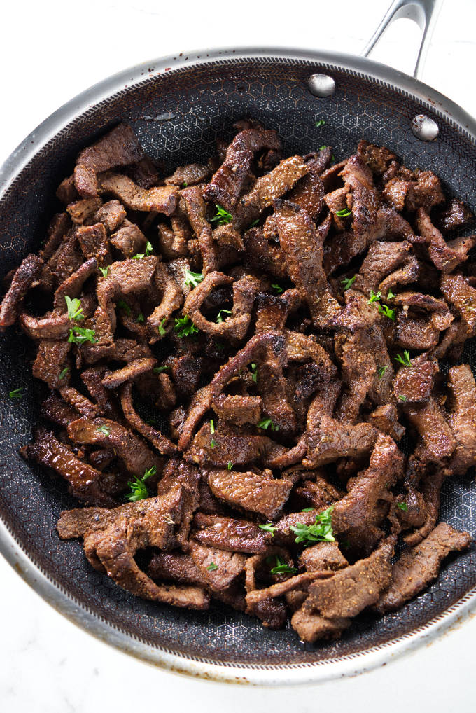 Seasoned steak strips in a saute pan.