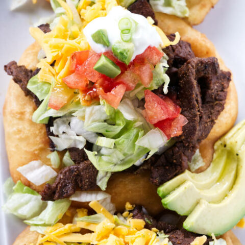 Three fry bread tacos topped with taco fixings.