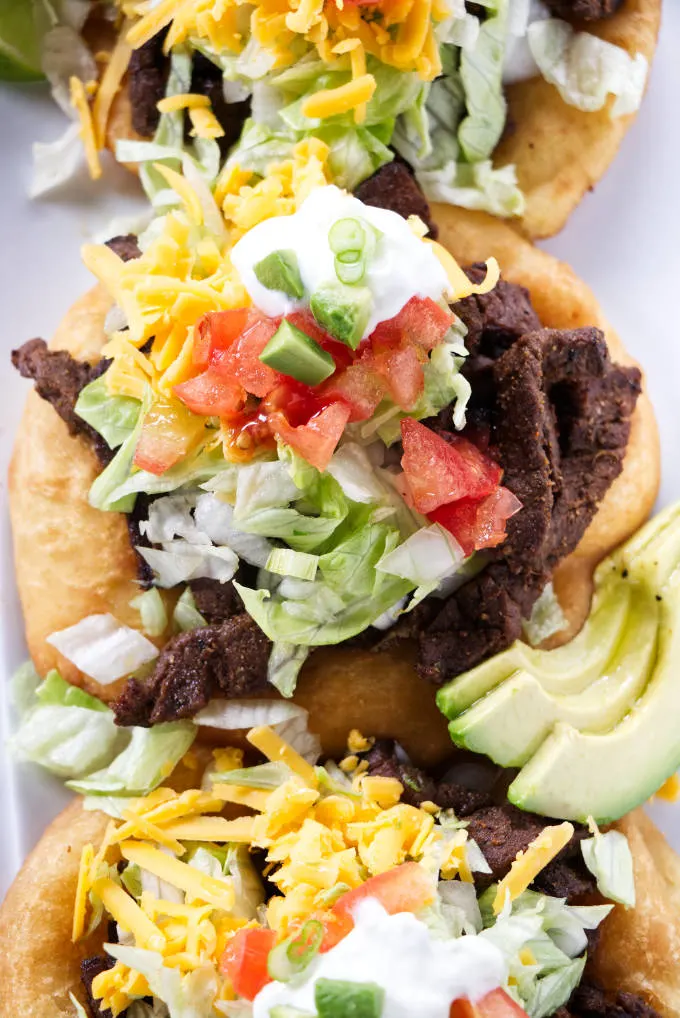 Three fry bread tacos topped with taco fixings.