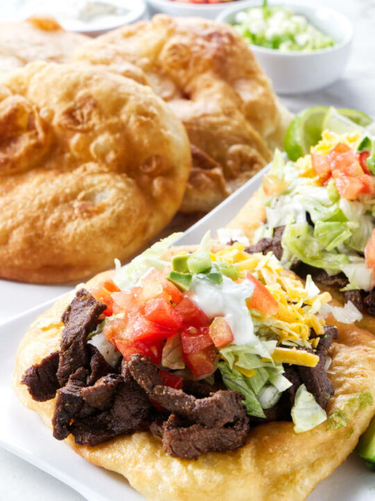 Two Indian fry bread tacos with fry breads in the background.