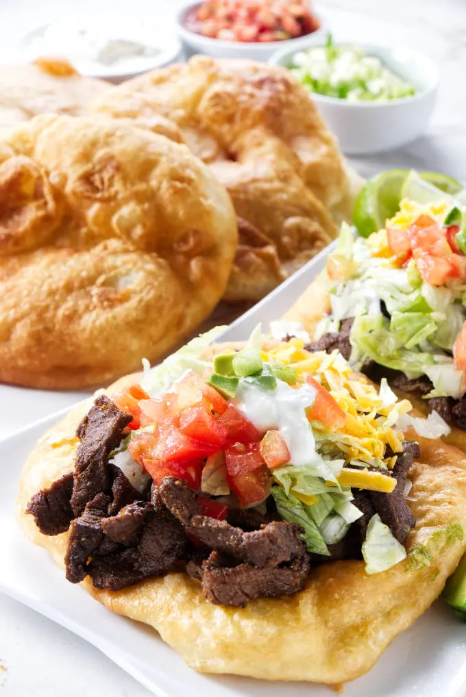 Two Indian fry bread tacos with fry breads in the background.