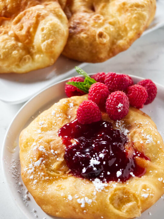 A fry bread topped with jam, raspberries, and powdered sugar.