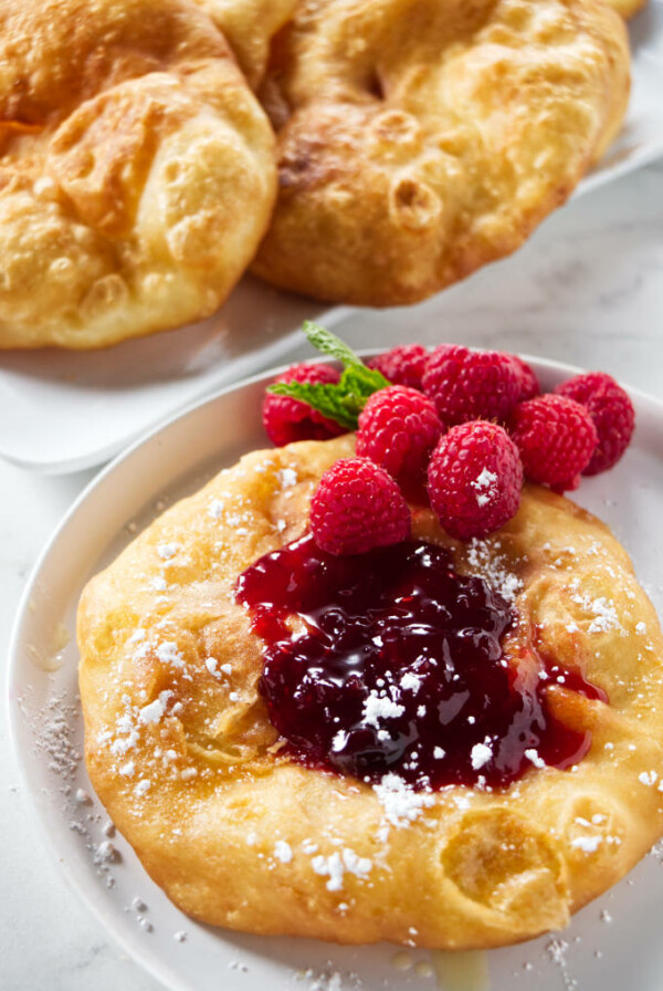 A fry bread topped with jam, raspberries, and powdered sugar.