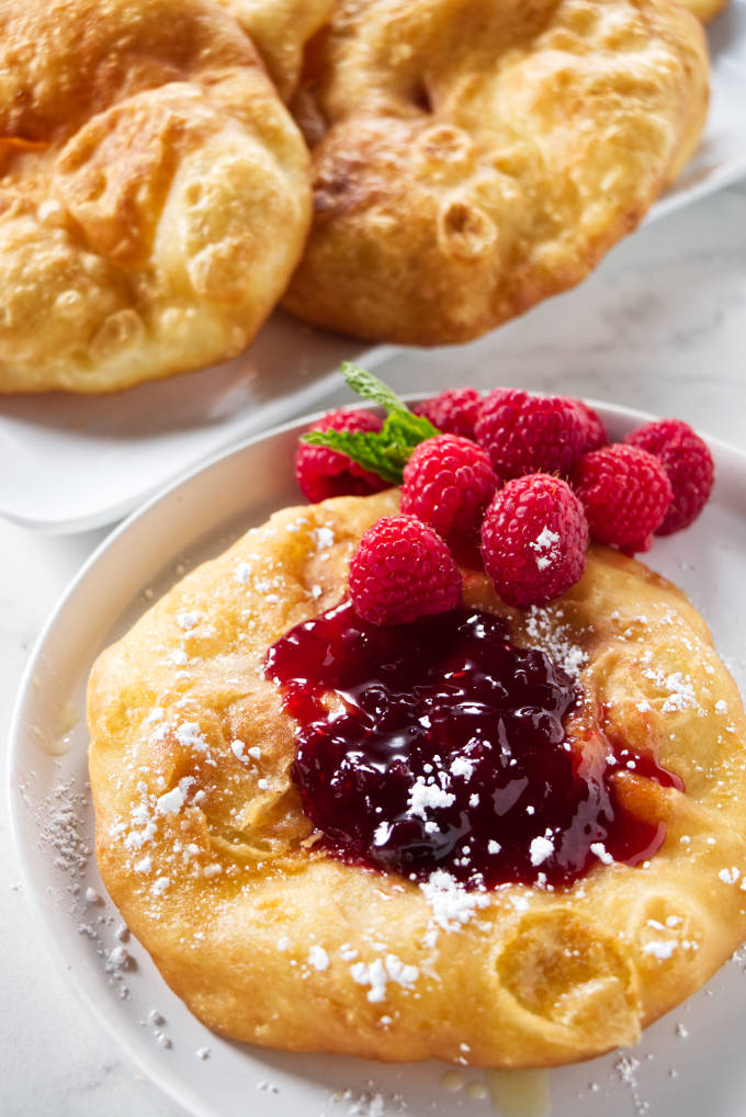 A fry bread topped with jam, raspberries, and powdered sugar.