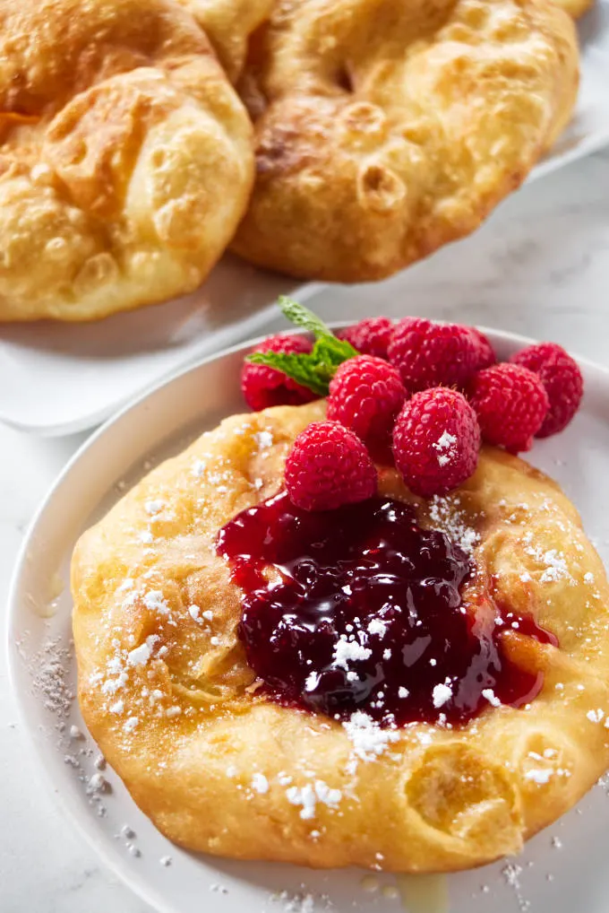A fry bread topped with jam, raspberries, and powdered sugar.