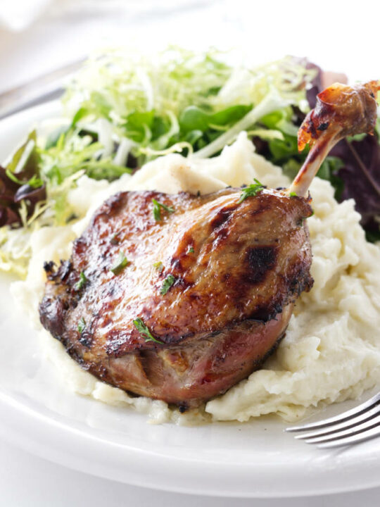Serving of duck leg confit with mashed potatoes and salad