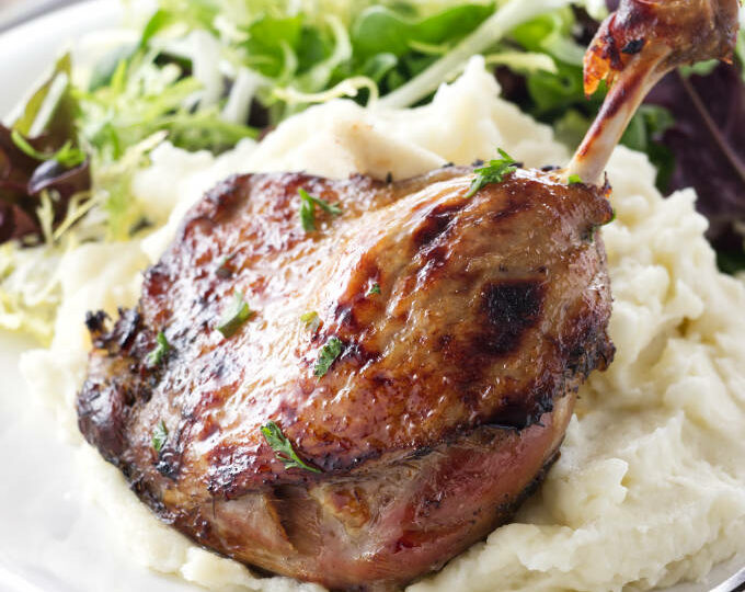 Serving of duck leg confit with mashed potatoes and salad