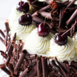 Dark cherries and chocolate rolls on a black forest cherry gateau cake.