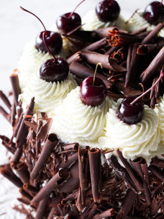 Dark cherries and chocolate rolls on a black forest cherry gateau cake.