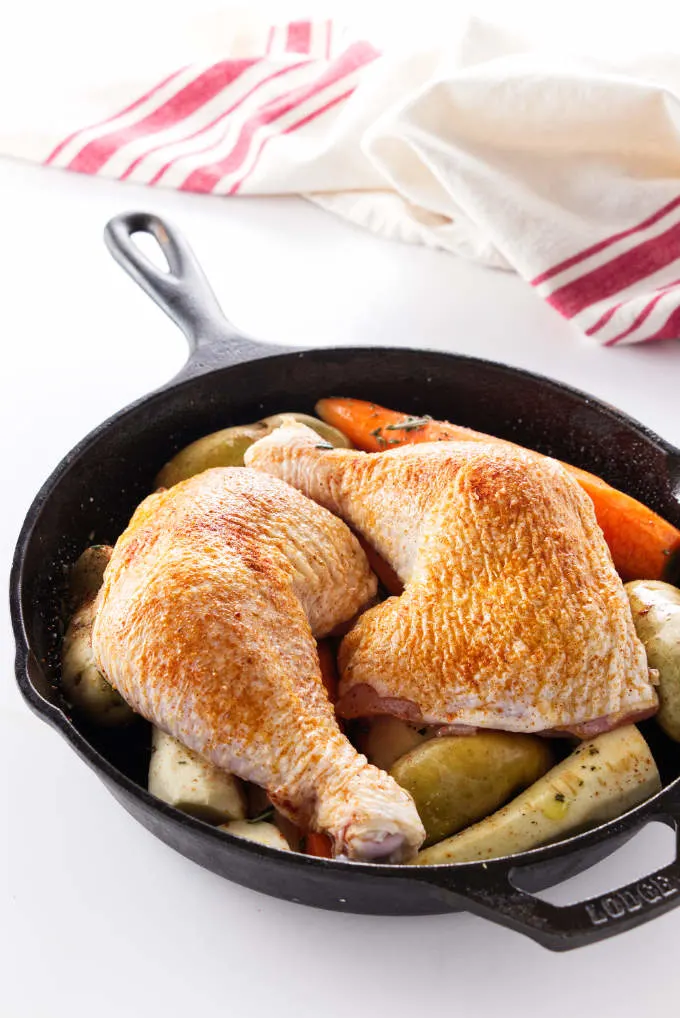 Chicken quarters and vegetables in a cast iron skillet.