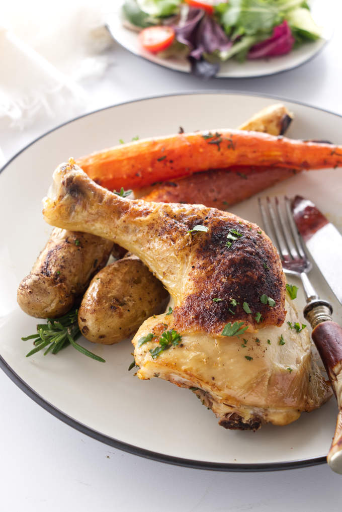 Roasted chicken quarters on a plate with veggies.