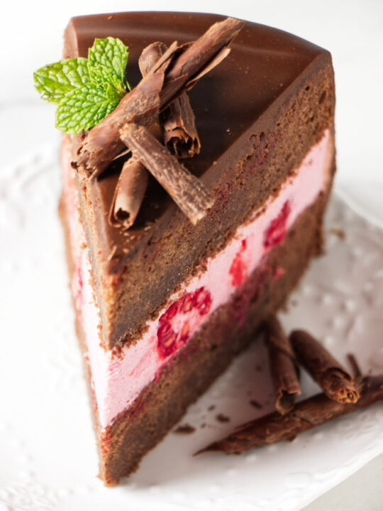 A slice of chocolate sponge cake filled with raspberry mousse cake filling.
