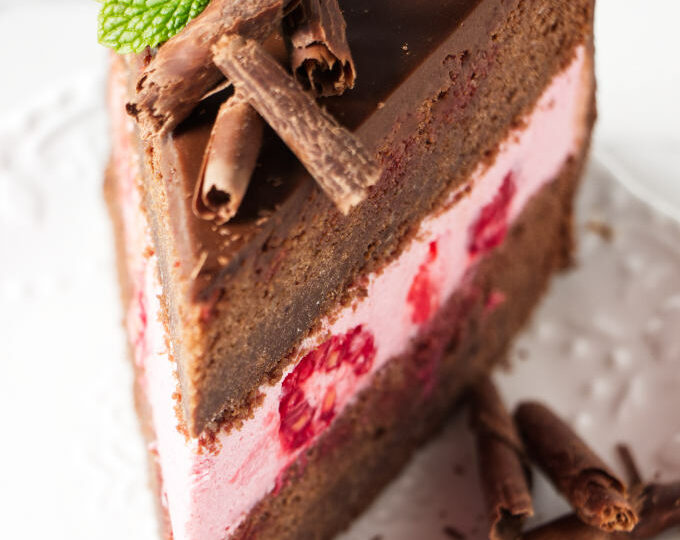 A slice of chocolate sponge cake filled with raspberry mousse cake filling.