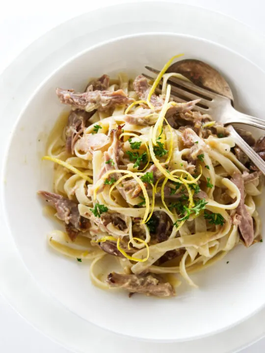 Overhead view of a serving of duck pasta, garnished with lemon zest and parsley