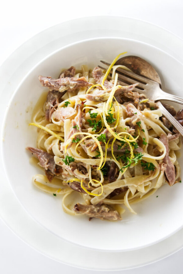 Overhead view of a serving of duck pasta, garnished with lemon zest and parsley