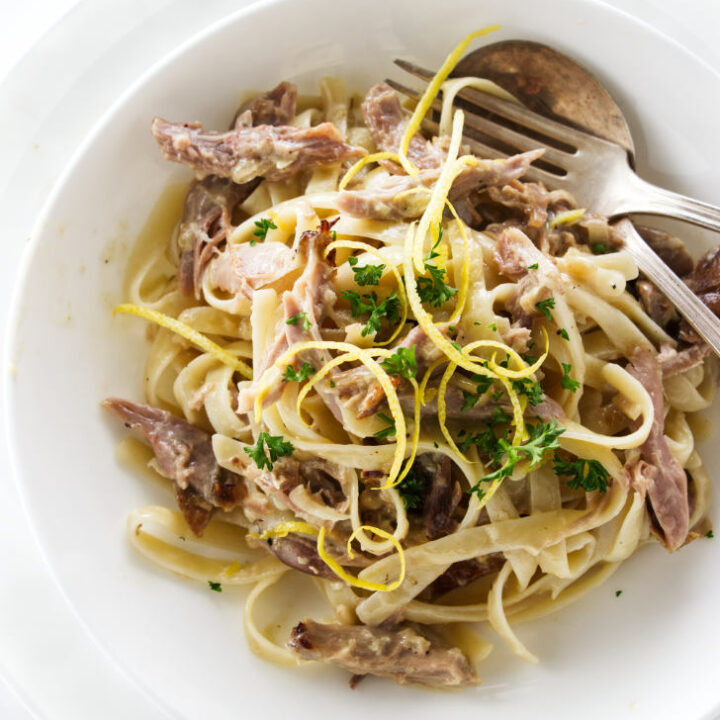 Overhead view of a serving of duck pasta, garnished with lemon zest and parsley