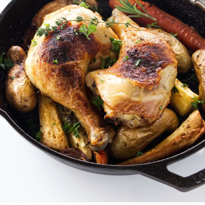 Chicken quarters and vegetables in a cast iron skillet.