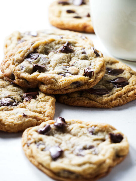 Several chocolate chip cookies next to a glass of milk.