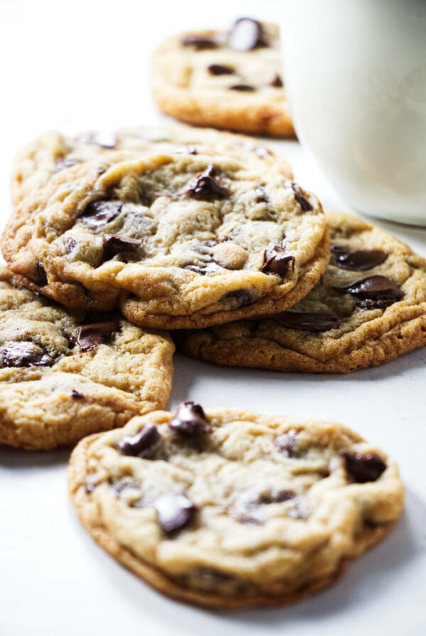 Several chocolate chip cookies next to a glass of milk.