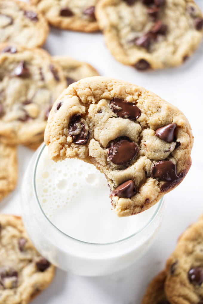 A chocolate chip cookie on the top of a glass of milk.