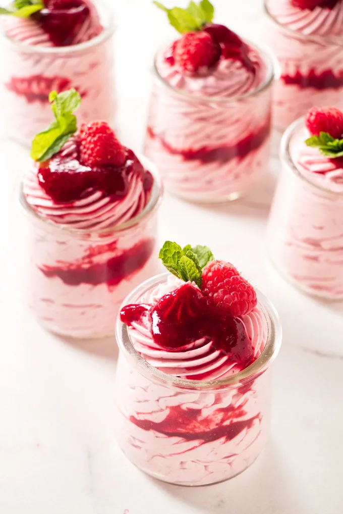 Several dessert cups with raspberry mousse decorated with raspberries and mint.