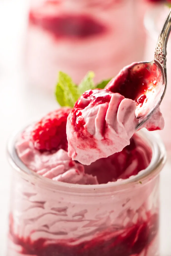 A spoon scooping raspberry mousse out of a dessert cup.