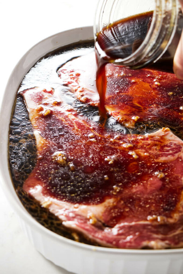 Pouring sake soy marinade over beef steaks.