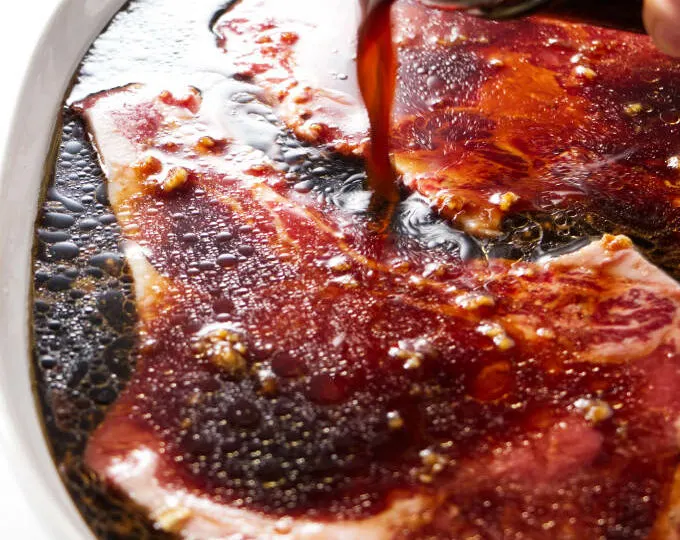 Pouring sake soy marinade over beef steaks.