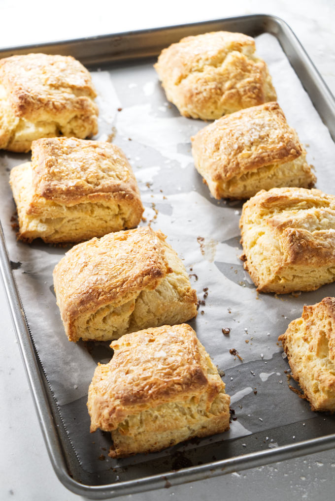 Eight sour cream biscuits on a hot baking sheet.
