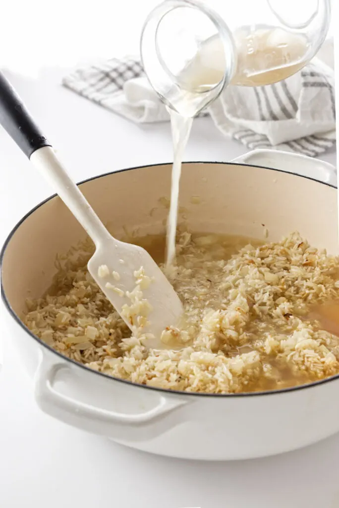 Pouring chicken broth into a skillet with basmati rice. 