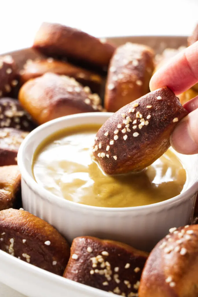 A pretzel bite being dipped in mustard sauce.