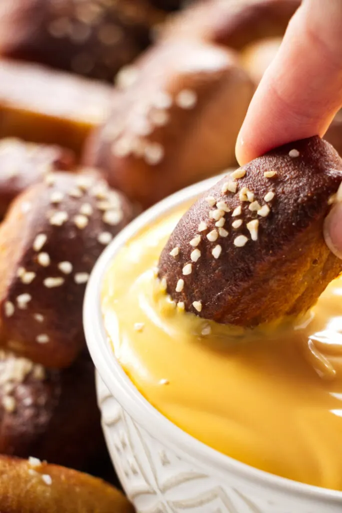 A pretzel bite being dipped in cheese sauce.