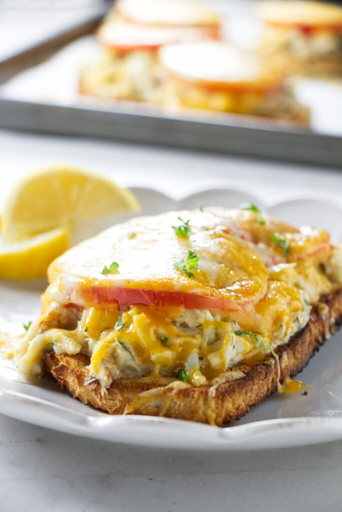 A crab melt sandwich on a plate with lemon wedges.