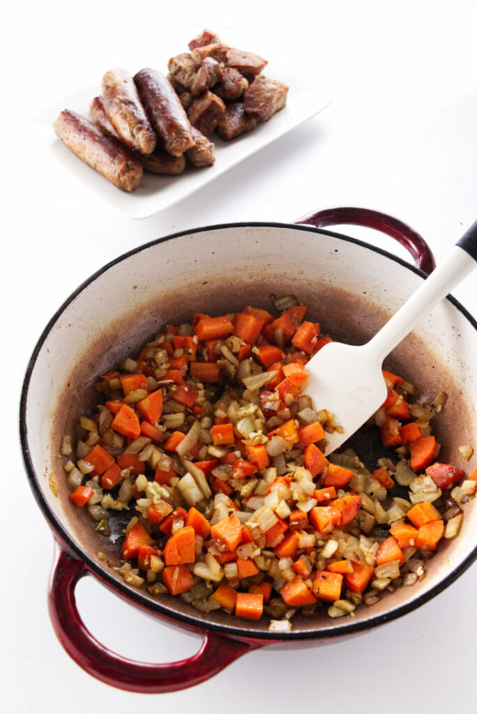 sauteed vegetables, browned sausage and pork in background