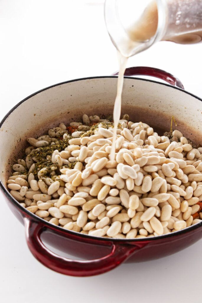 broth being poured over beans for cassoulet