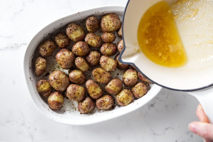 Pouring garlic butter over a pan of roasted baby potatoes.