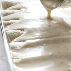 Pouring white enchilada sauce over enchiladas.