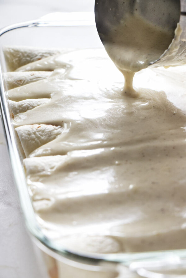 Pouring white enchilada sauce over enchiladas.