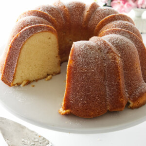 Cold oven pound cake on a pedestal, server in forground and flowers in background