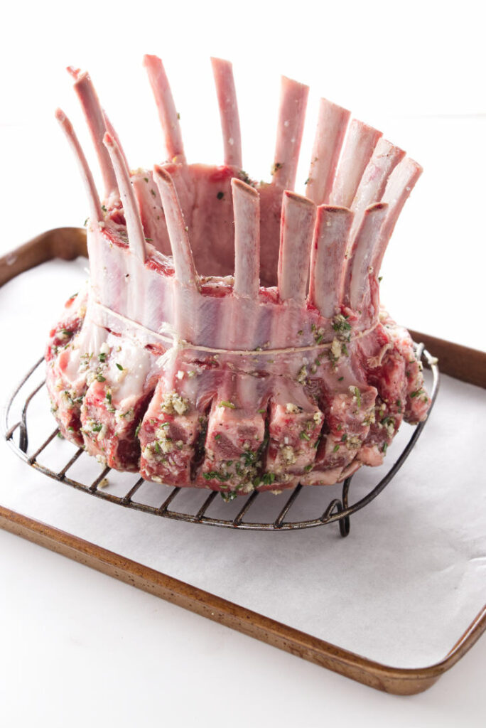 An uncooked crown rack of lamb on a baking sheet.