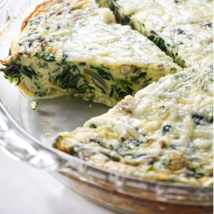A closeup of a quiche with spinach and mushrooms.