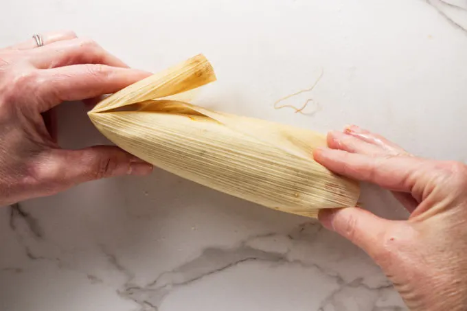 Folding the end of a corn husk over a tamale.