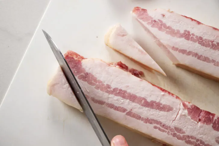 Cutting fat off the ends of bacon strips.