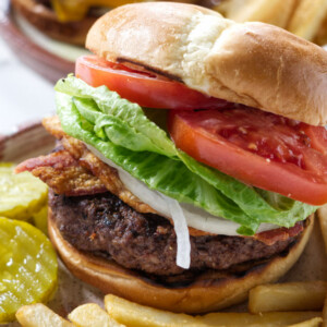 Two venison burgers assembled with lettuce, onions, and tomatoes.