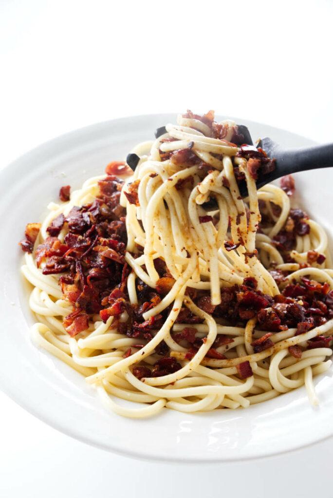 Mixing carbonara ingredients into a bowl of pasta.
