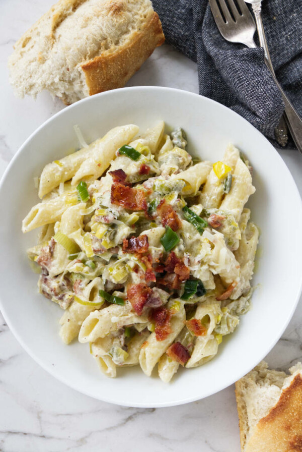 A dish of pasta with bacon bits on top.