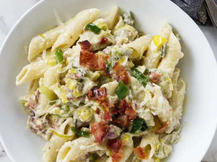 A dish of pasta with bacon bits on top.