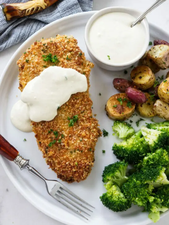 A breaded and baked chicken breast on a plate with sauce.