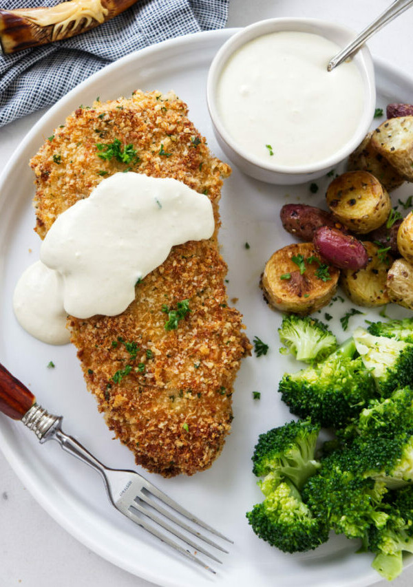 A breaded and baked chicken breast on a plate with sauce.