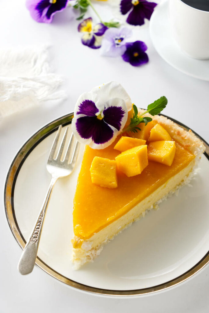 A slice of mango tart next to flowers and coffee.